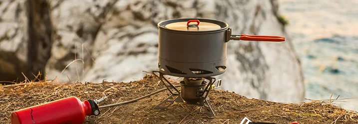 Ein Gaskocher mit Topf und roter Brennstoffflasche am Meer.
